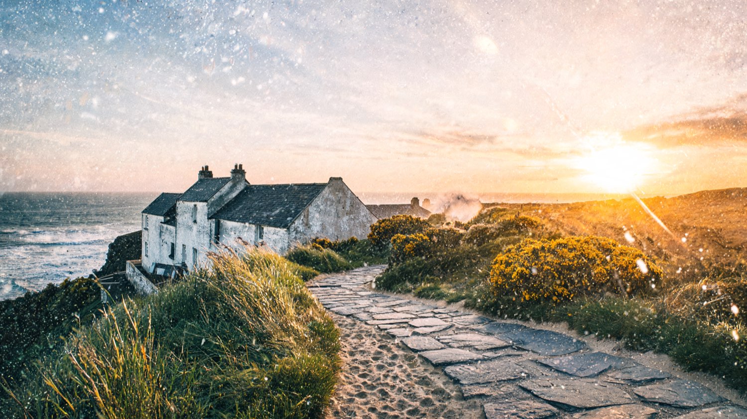 Whitewashed stone resort building on a grassy Cornwall clifftop at golden hour above a slate-blue sea